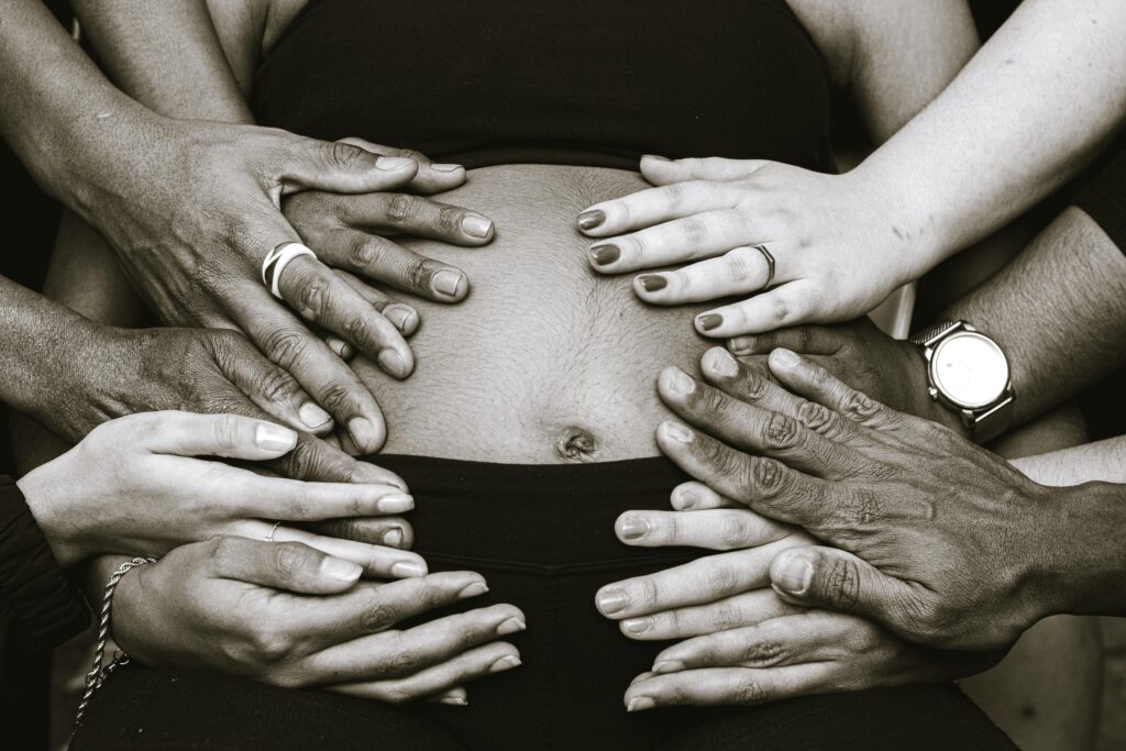 Black and white hands of anonymous multiracial people touching bare belly of faceless pregnant woman while anticipating birth of baby