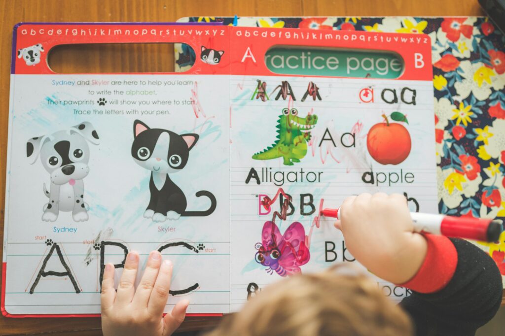 Child practicing writing with a workbook and marker, learning the alphabet creatively.